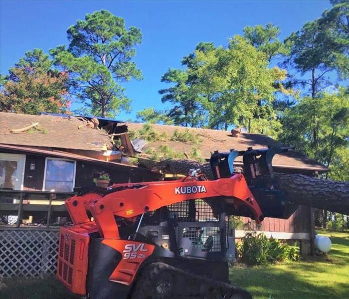 a large tree fell on the roof of a home splitting it in half, a tractor is removing it